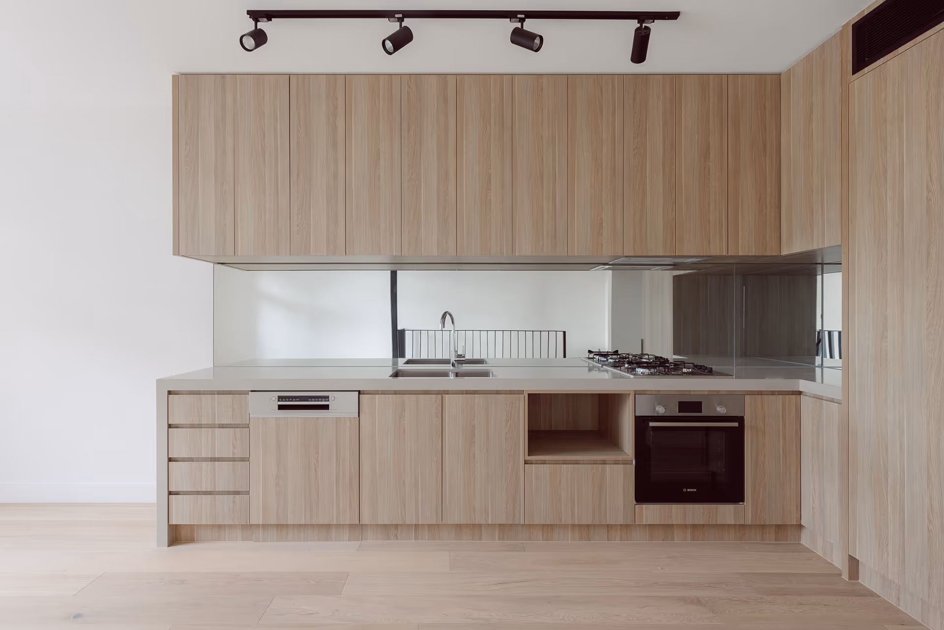Modern kitchen with light wood cabinets, built-in oven, gas stove, dishwasher, and a double sink under a mirrored backsplash.