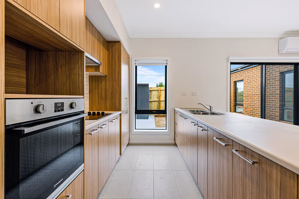 Modern kitchen with wooden cabinets, built-in oven, stovetop, and large white countertop with sink under natural light from windows.