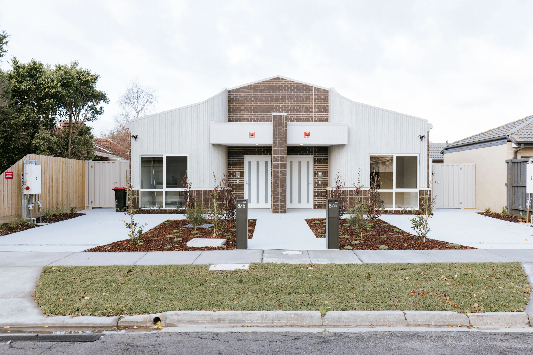 Pair of new brick and white-clad homes with matching front doors and landscaped gardens, built by Harnest