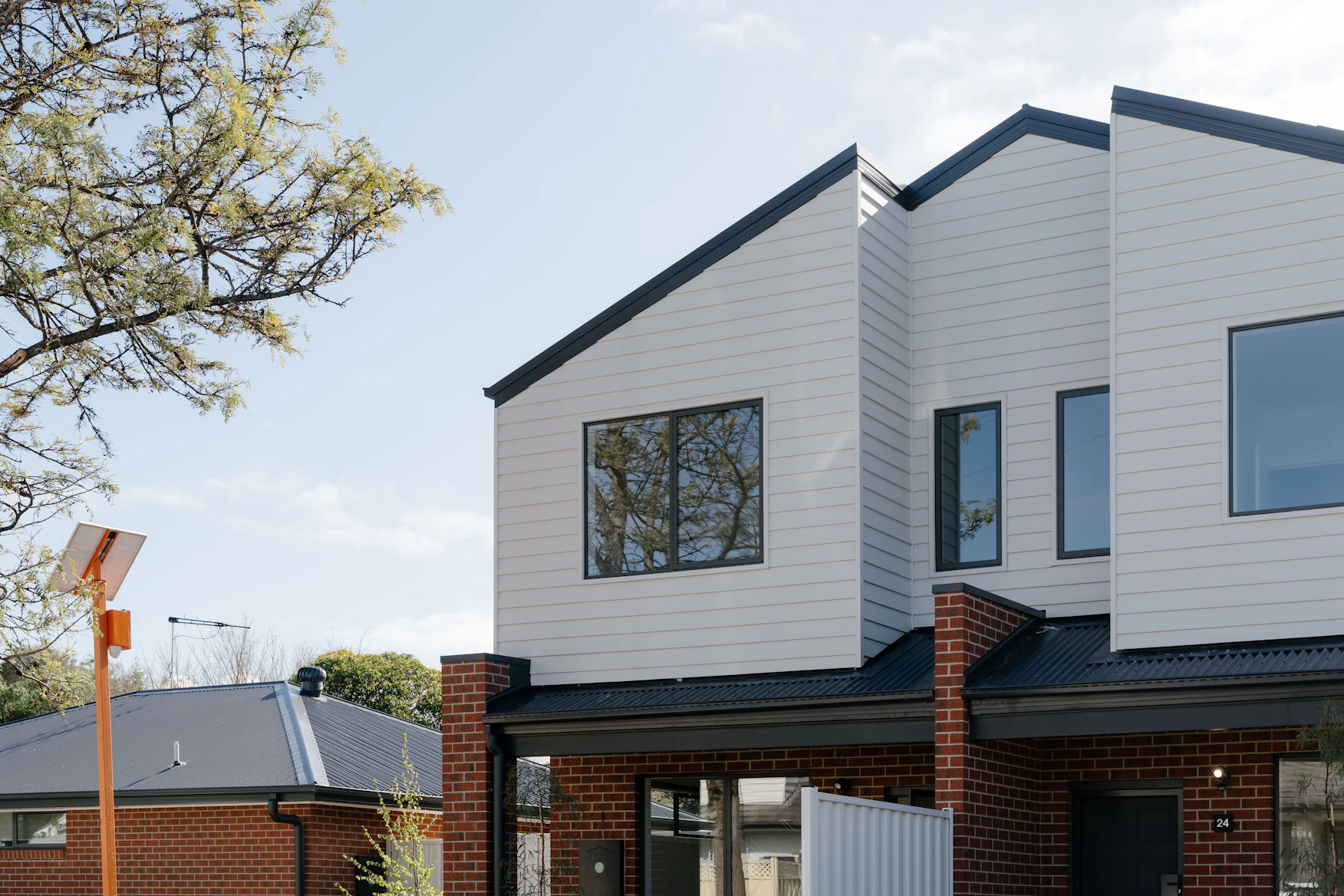 Two-storey townhouses with white cladding and red brick, built by Harnest