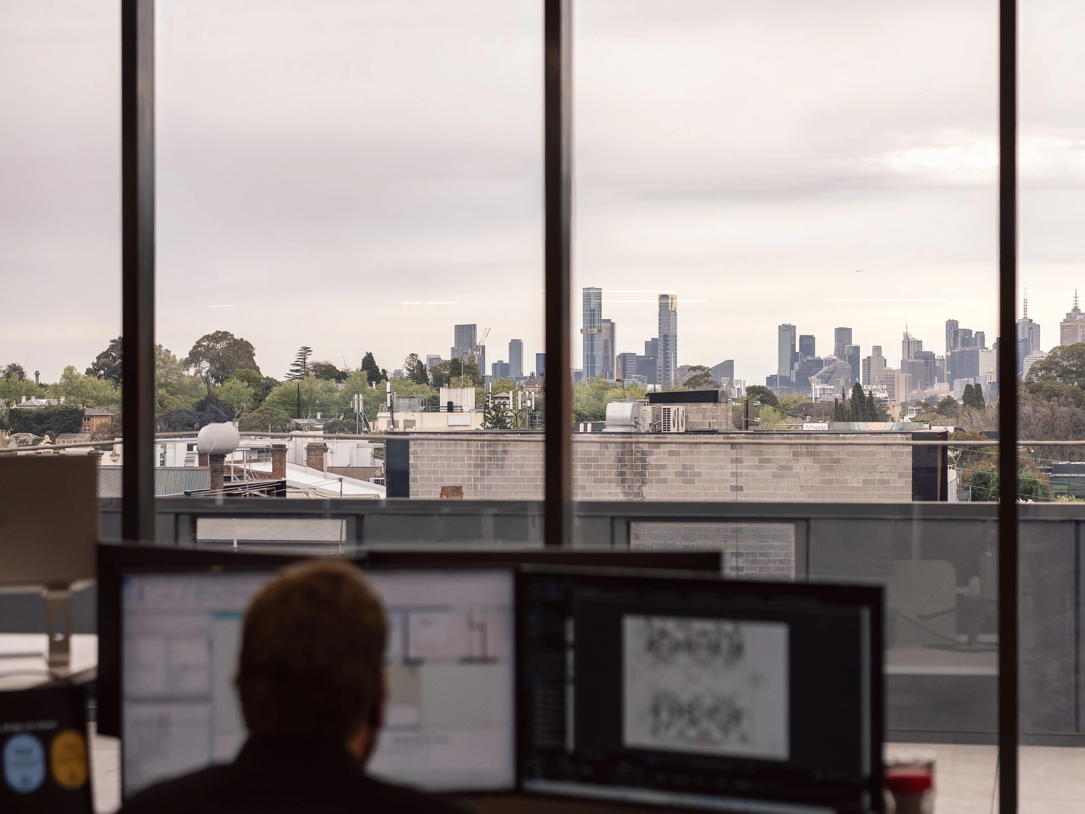 Team member working at a computer with a view of the Melbourne city skyline through the office windows