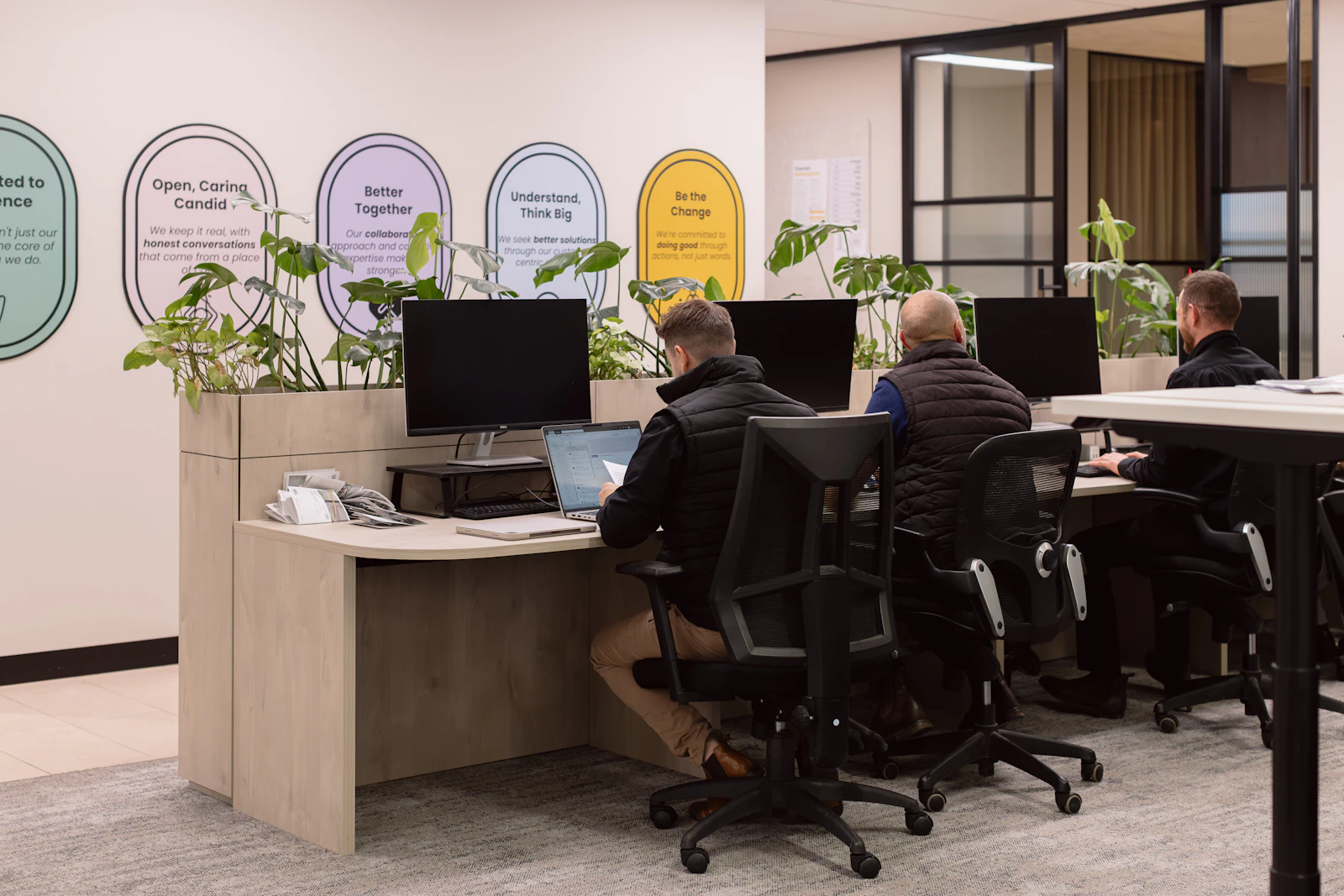 Harnest team members working at desks in an office with plants and company values on the wall
