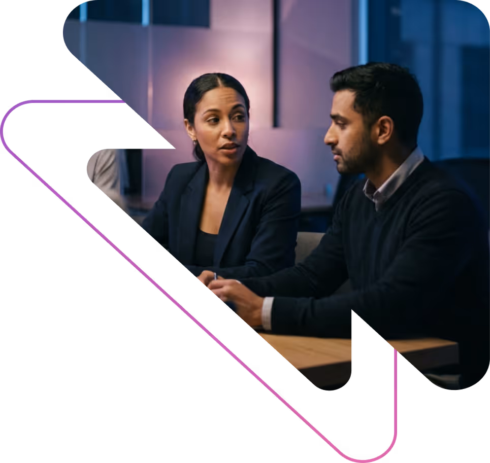 Two professionals engaged in a serious conversation at a meeting table in an office with modern lighting.