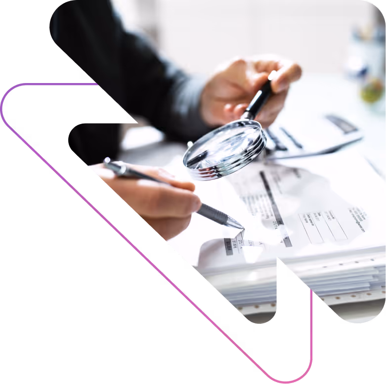 Person examining documents with a magnifying glass and pen, focusing on financial or regulatory details.