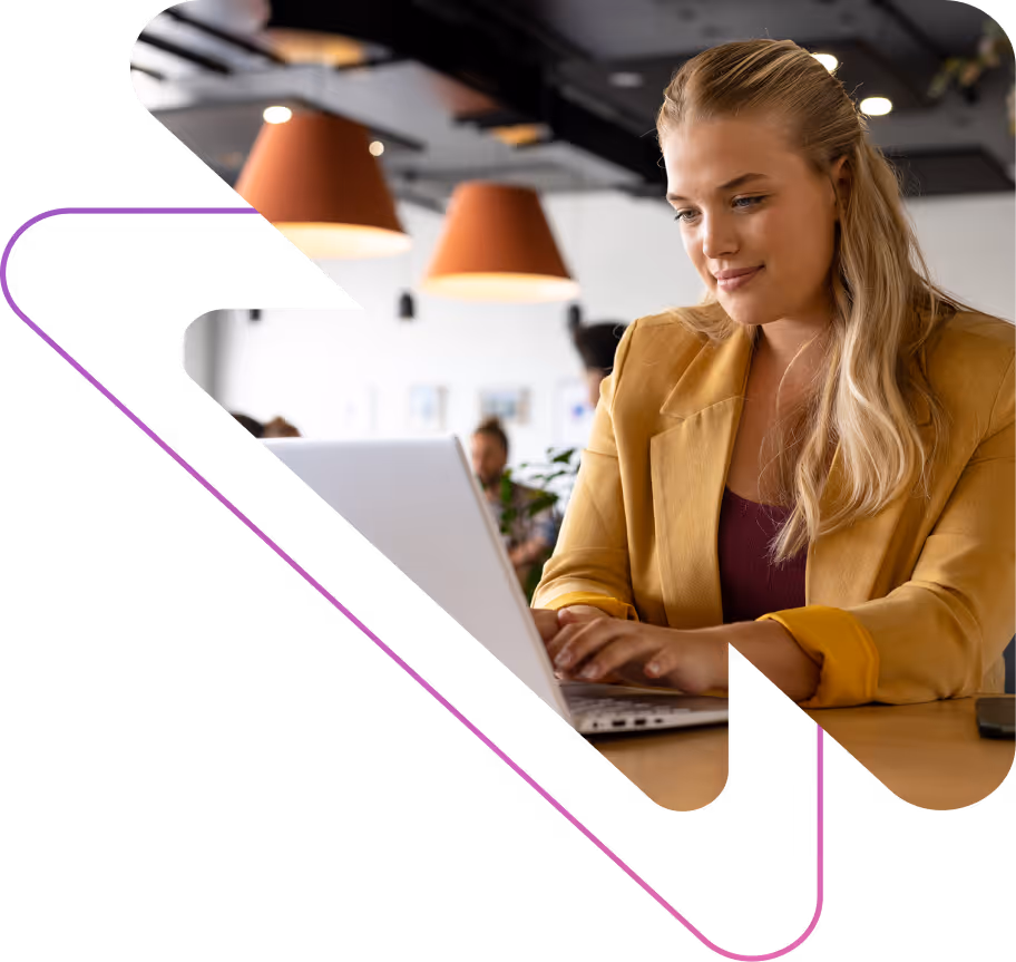 Young woman with blonde hair wearing a yellow blazer working on a laptop in a modern office with pendant lights.