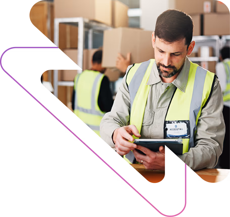 Warehouse worker in high-visibility vest using a tablet with shelves and boxes in the background.