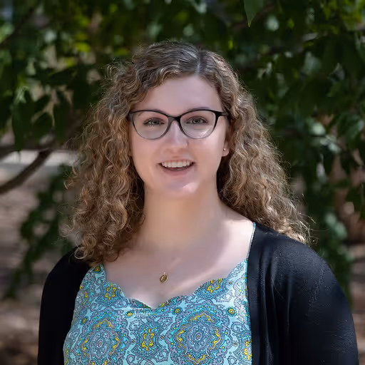 A woman wearing glasses standing under a tree.