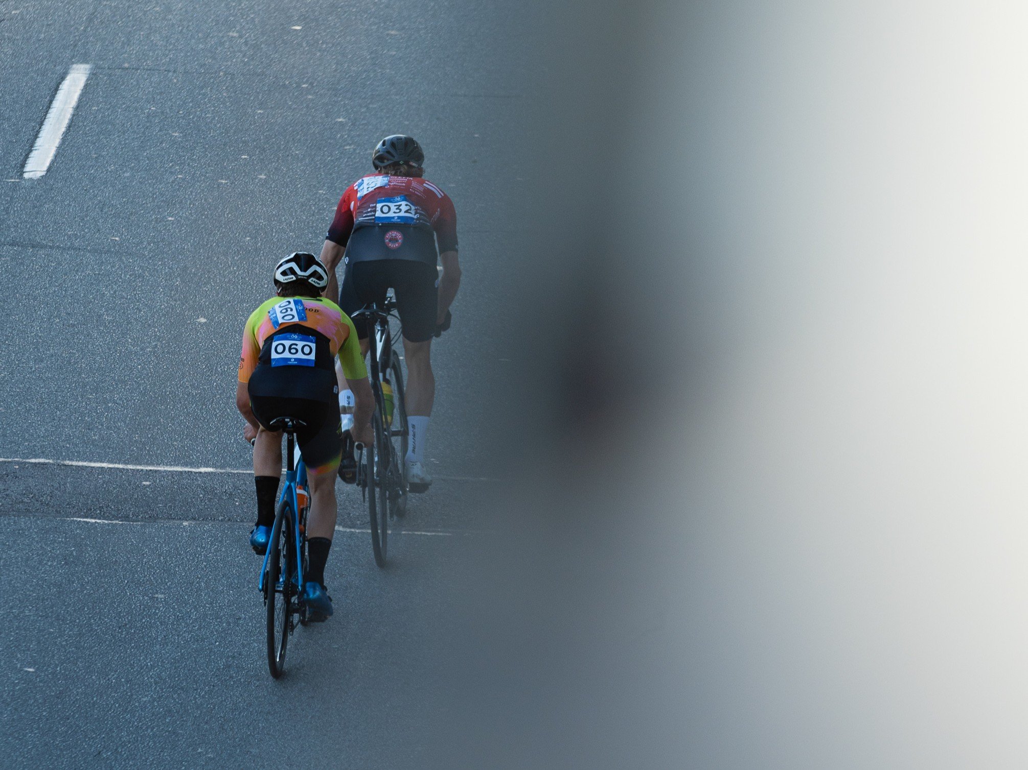 Two cyclists wearing numbered race jerseys riding on a paved road.