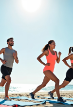 Three masked cleaning staff mopping the floor in a living room with a gray sofa and plant.