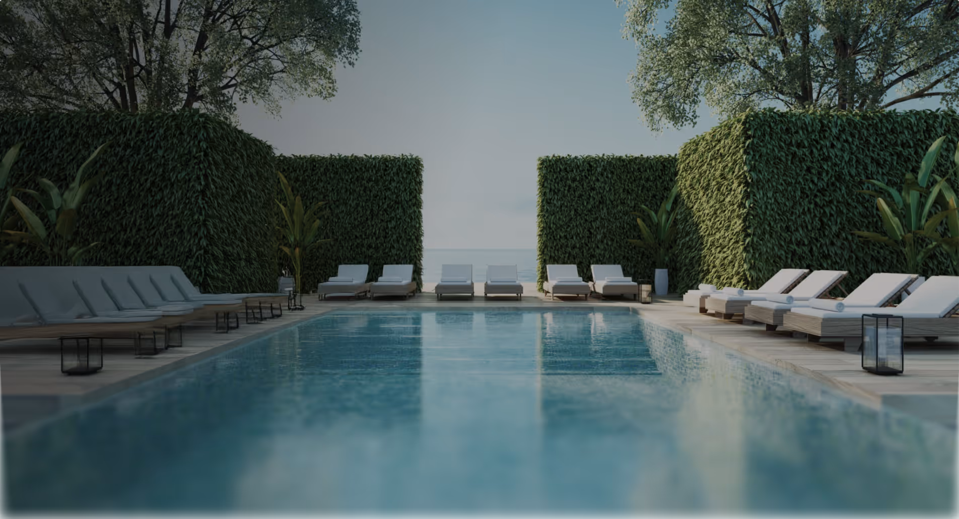Piscine extérieure entourée de chaises longues blanches et de murs végétaux avec des arbres en arrière-plan.