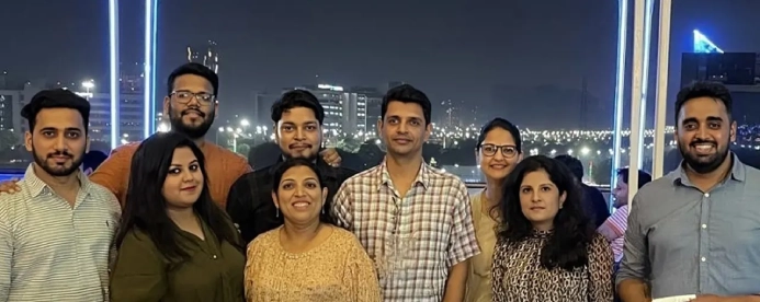 A diverse group of ten people smile for a photo at night with city lights and illuminated structures in the background.