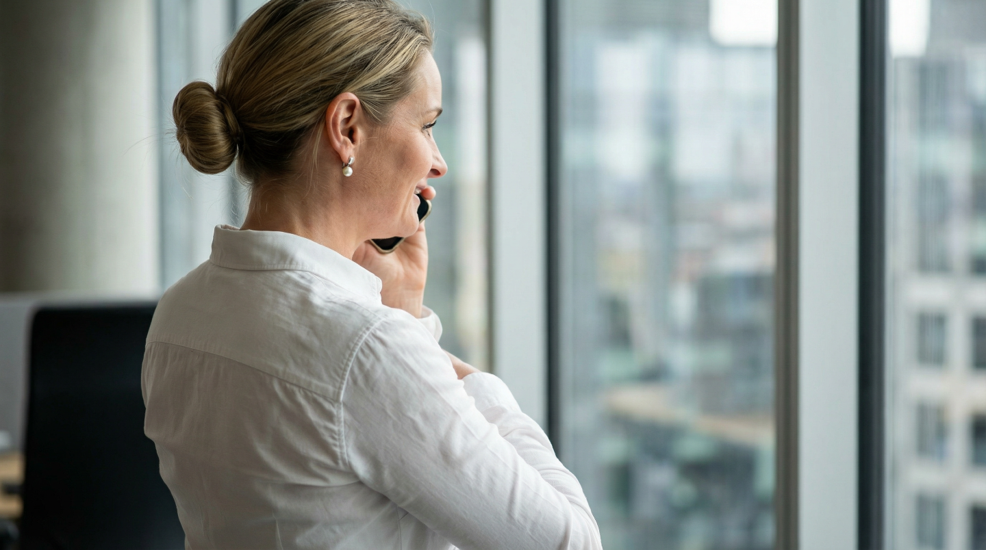 Frau mit Brille und blauem Pullover unterzeichnet Dokumente an einem Schreibtisch mit Ordnern und Stempeln.