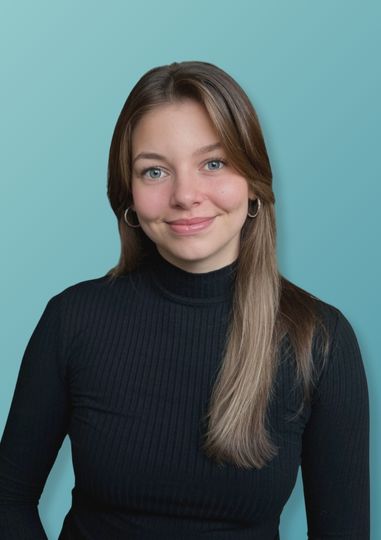 Junge Frau mit langen braunen Haaren in schwarzem, geripptem Rollkragenpullover vor hellblauem Hintergrund.