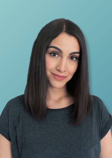 Junge Frau mit glatten, schulterlangen dunklen Haaren, trägt ein dunkelgraues T-Shirt vor hellblauem Hintergrund.