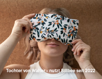 Frau hält ein weißes Kissen mit floralem Muster vor Gesicht, braune Wand im Hintergrund.