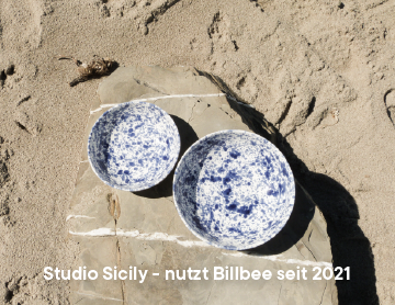 Zwei blaue und weiße Keramikschalen auf einem Stein im Sand liegend.