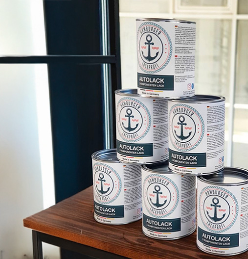 Sechs Dosen Hamburger Autolack, stapelt auf einem Holztisch vor einem Fenster.