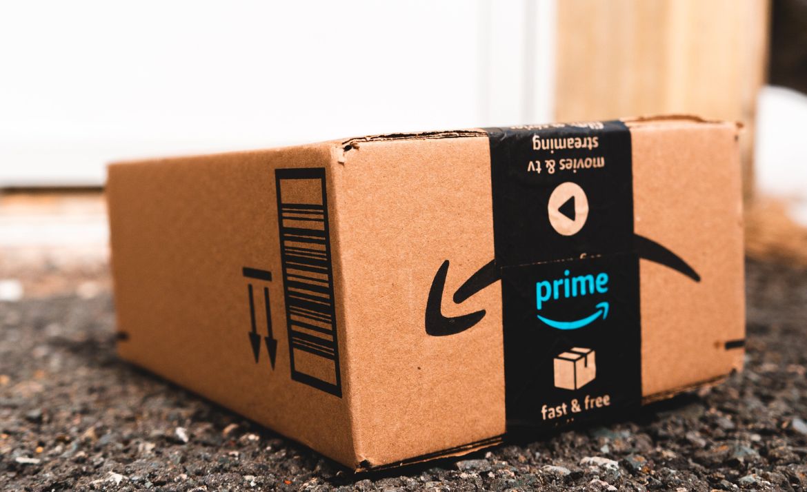 Amazon Prime Paket mit schwarzem Klebeband und Aufschrift 'prime fast & free' auf Asphaltboden