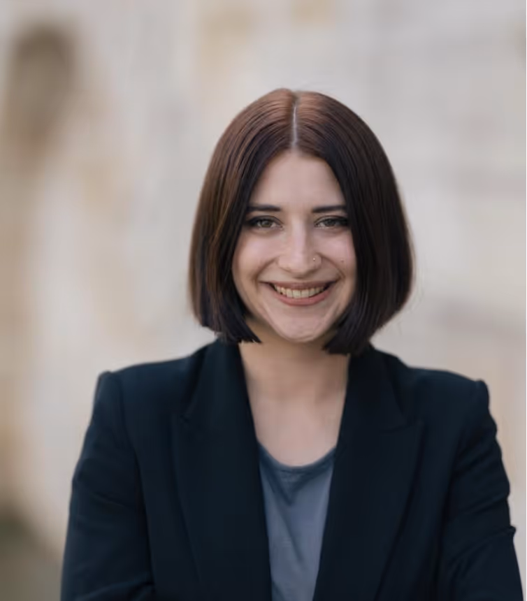 Porträt einer lächelnden jungen Frau mit kurzem braunen Haar, die einen schwarzen Blazer trägt.