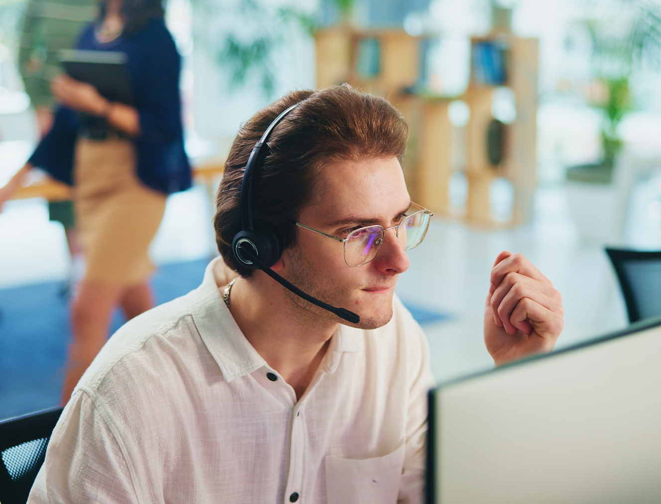 Homme portant un casque audio avec micro, travaillant devant un écran en bureau lumineux.