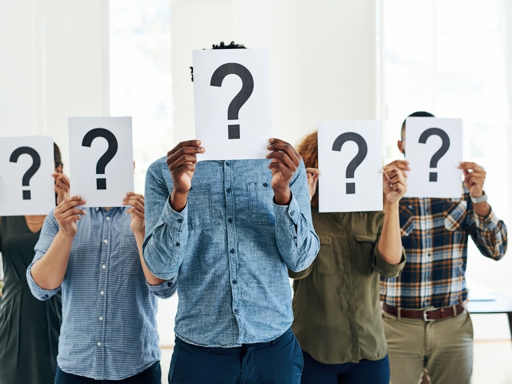 A group of people holding question mark cards in front of their face.