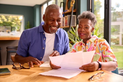 Senior Couple Smiling, Reviewing Paperwork Indoors at Home