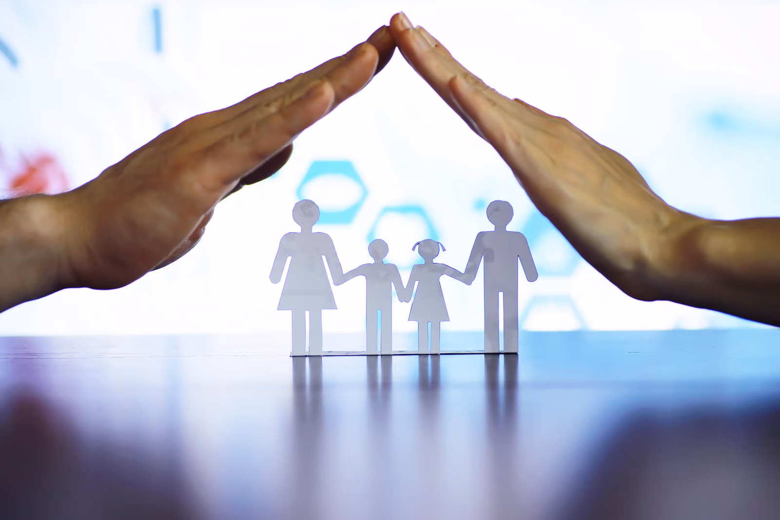 Two hands create a protective roof over a paper cut-out family of four.