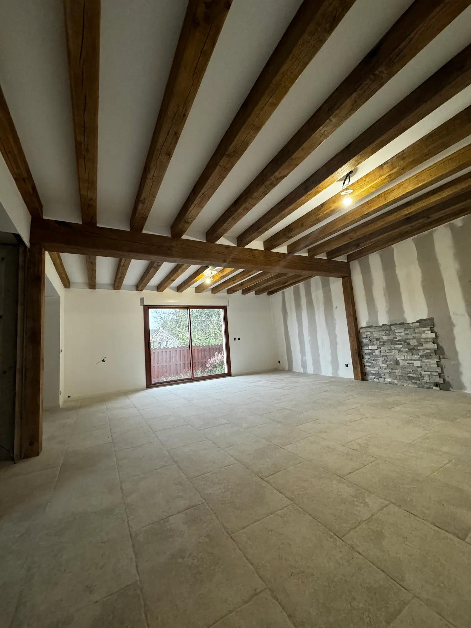 Pièce rénovée avec poutres apparentes, carrelage et mur en pierre