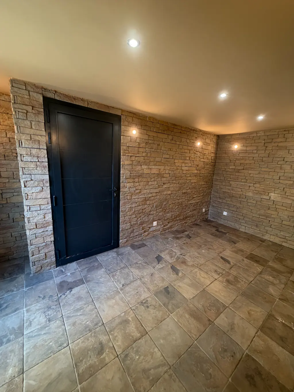 Entrée avec parement en pierre naturelle, carrelage et porte noire