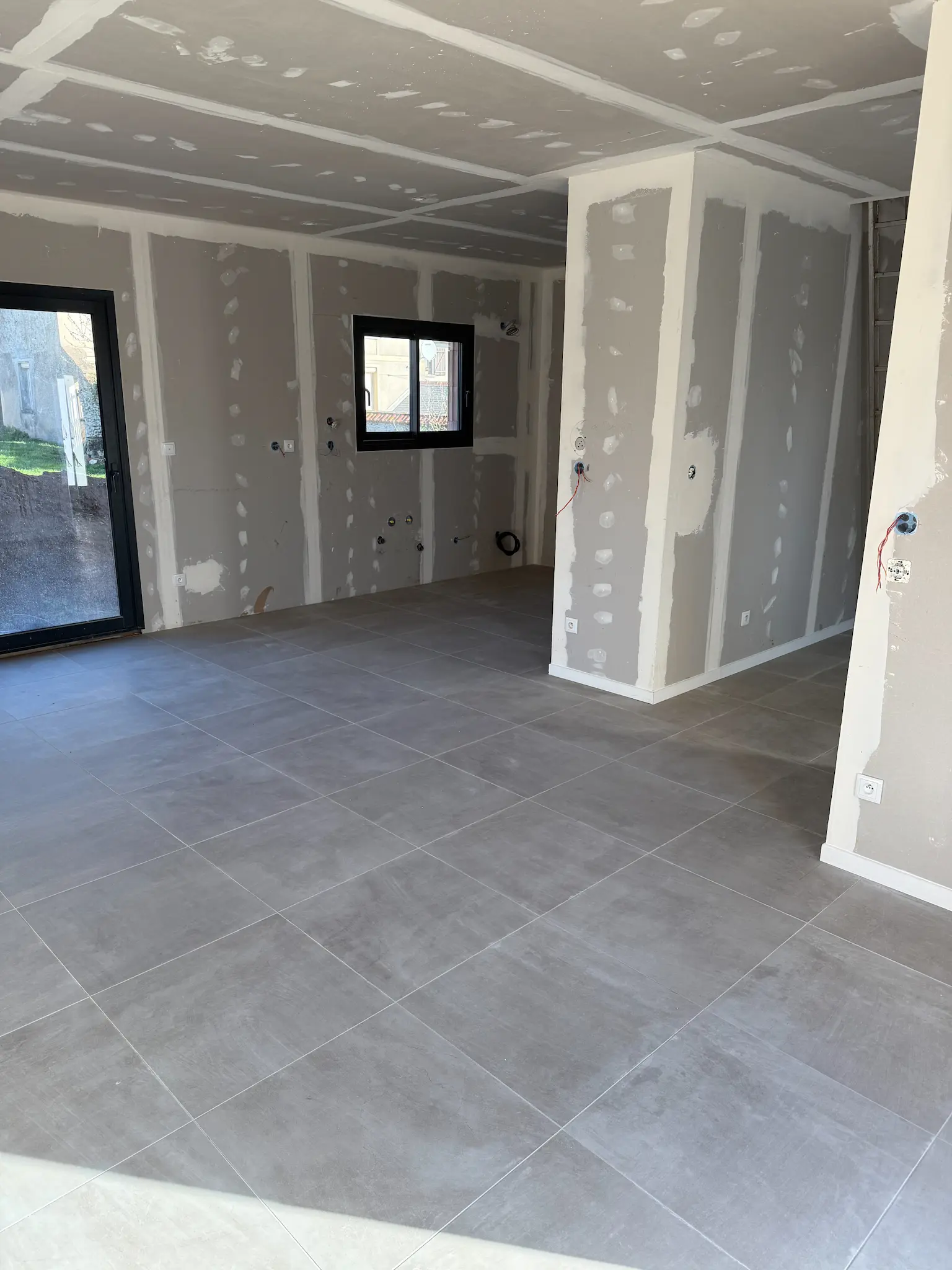 Pose de carrelage gris grand format dans une pièce en cours de finition