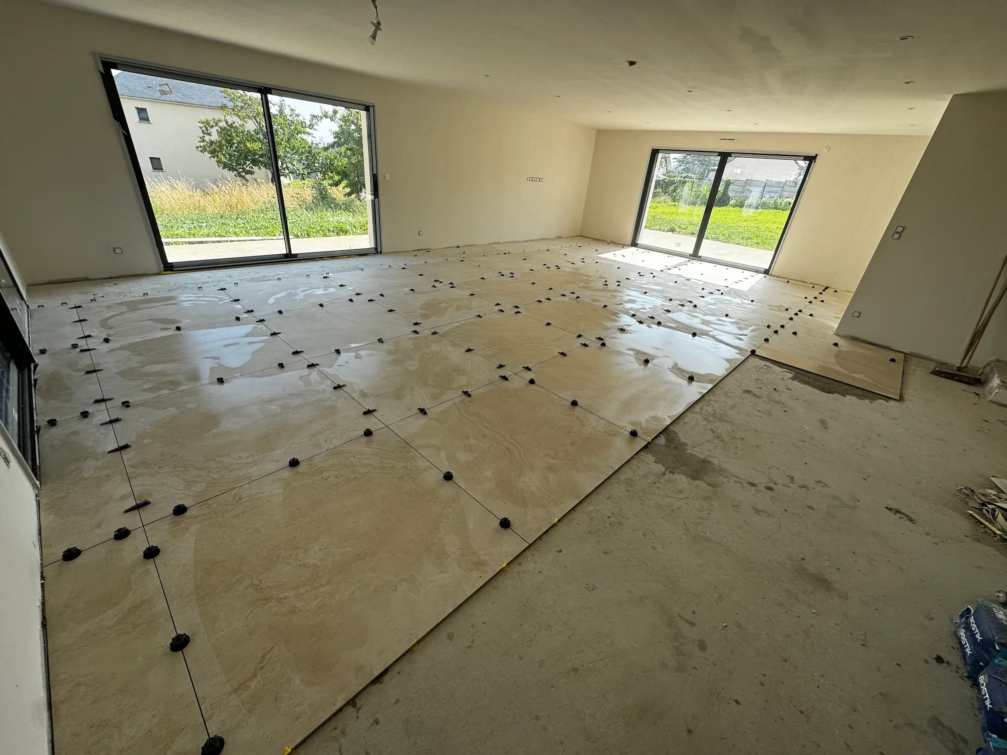 Pose de carrelage grand format en cours dans un séjour neuf
