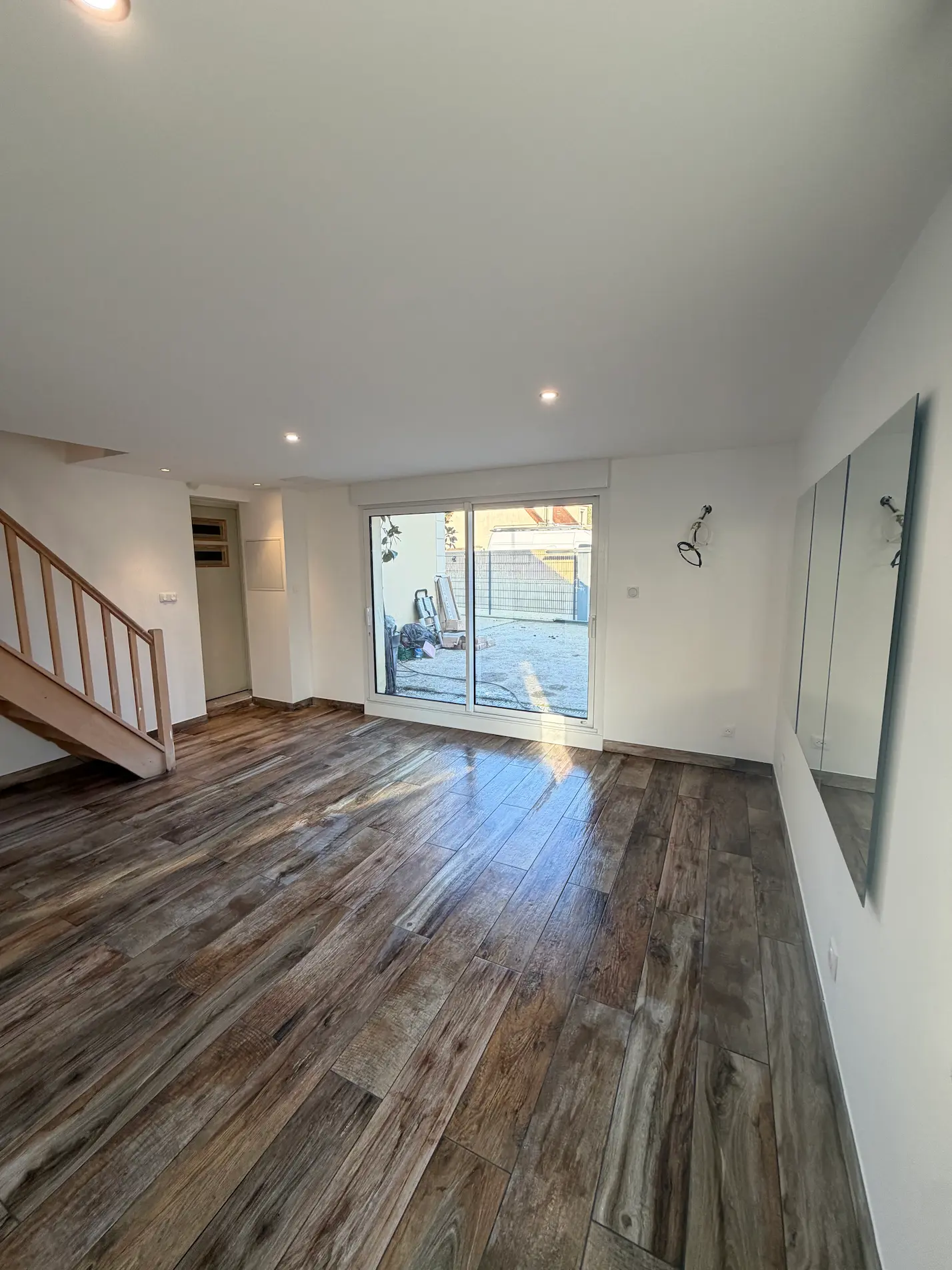 Pièce de vie rénovée avec carrelage imitation bois, miroirs muraux et spots encastrés