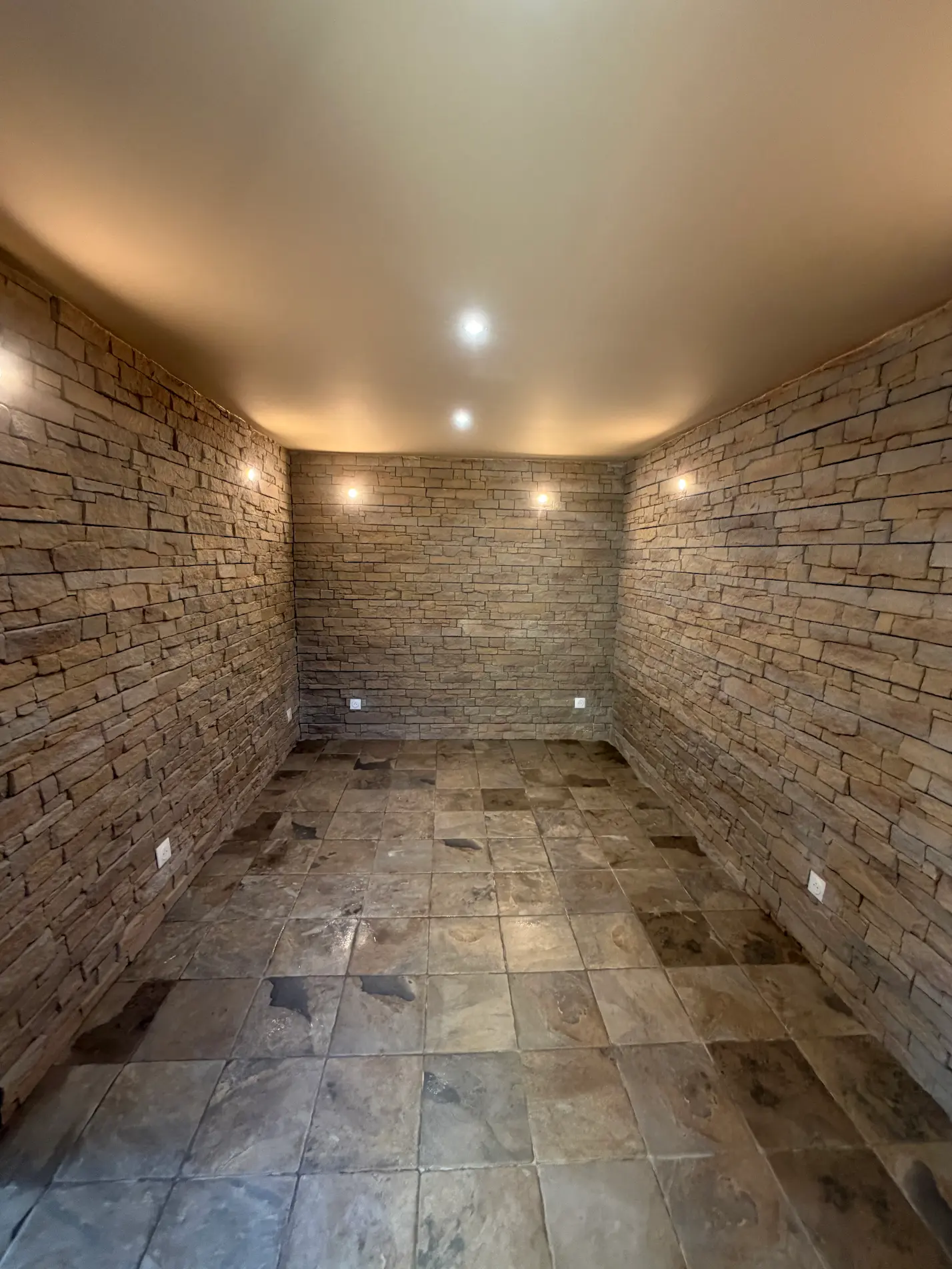 Cave aménagée avec parement pierre naturelle, carrelage en pierre et éclairage encastré