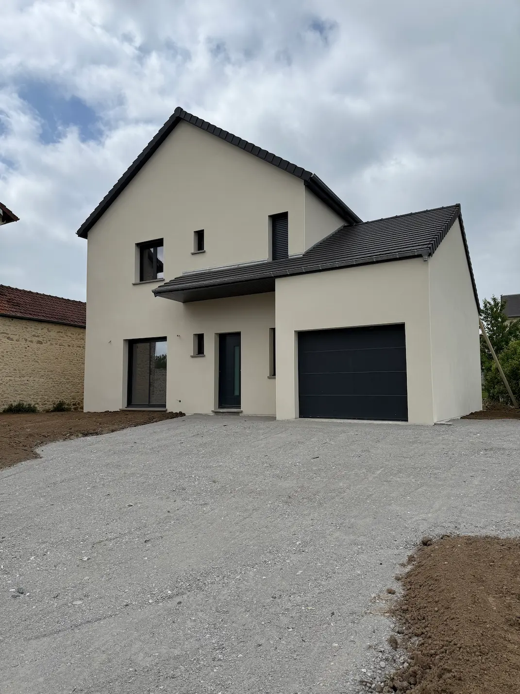 Maison neuve terminée avec façade blanche, toiture grise et allée pavée