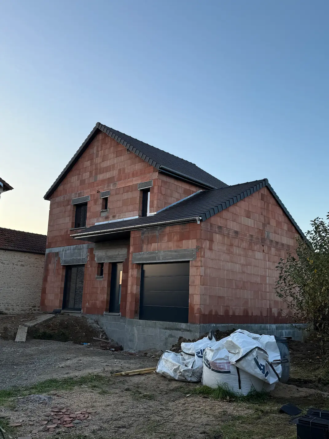 Maison en briques en cours de construction avec matériaux de chantier à l'entrée