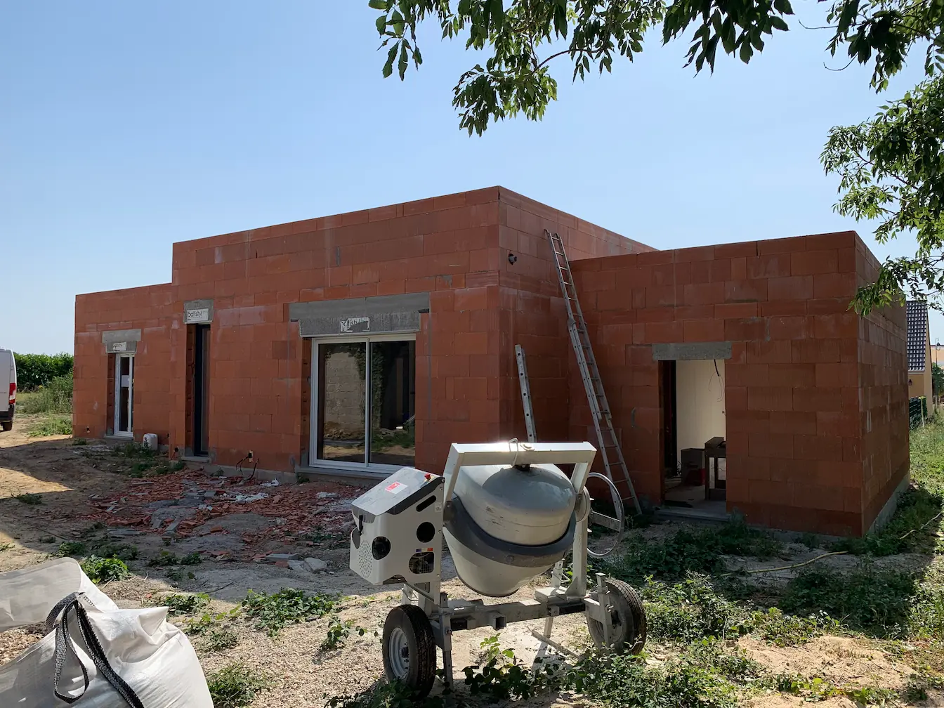 Chantier en cours avec matériaux et bétonnière devant la structure en briques