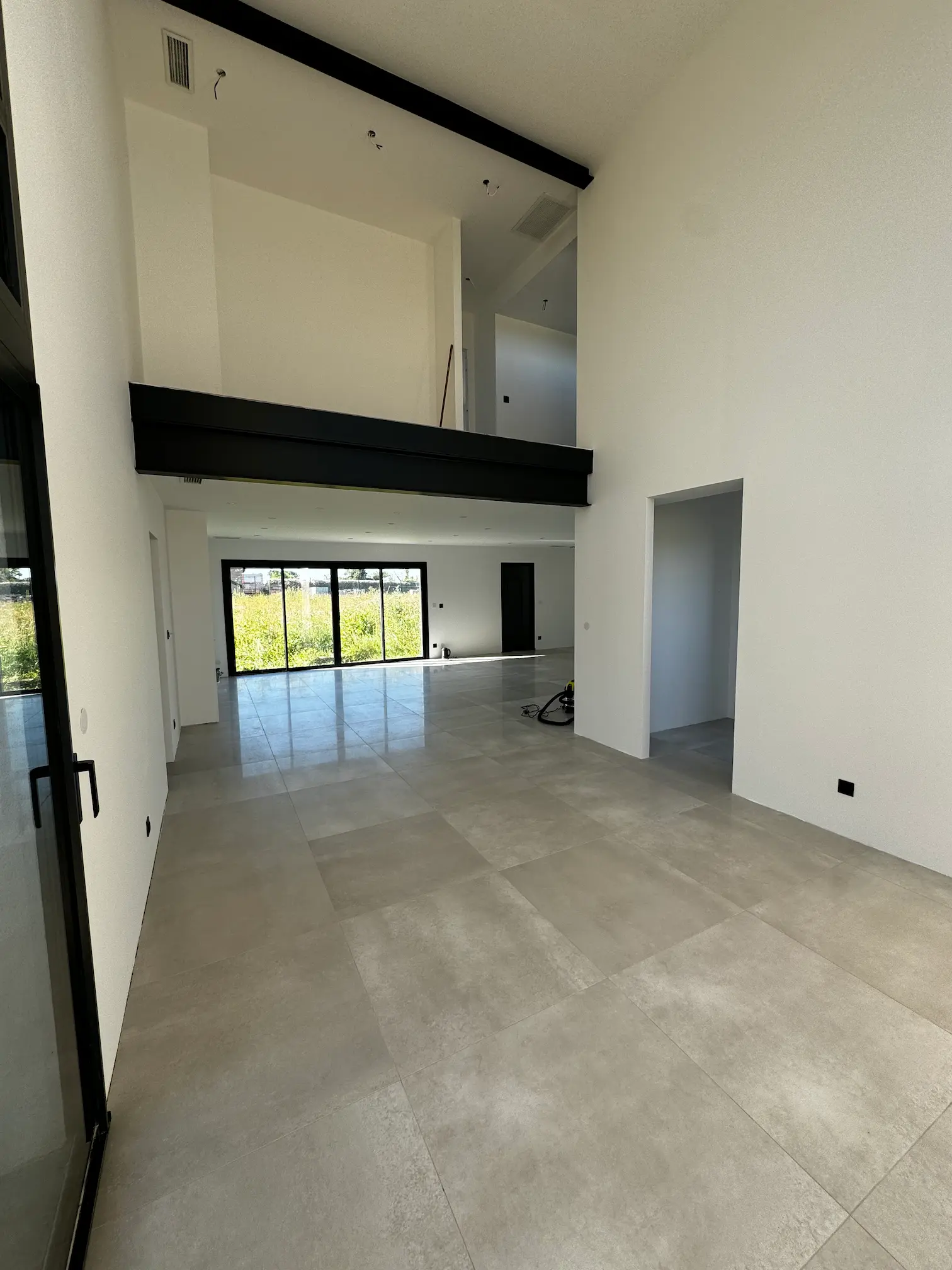 Pièce de vie ouverte avec grandes baies vitrées, carrelage gris et volumes contemporains