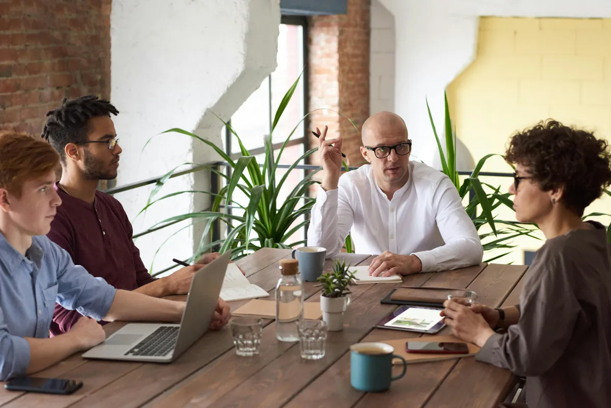Team in a bright loft office debating ideas at a table with a laptop, refining their value proposition