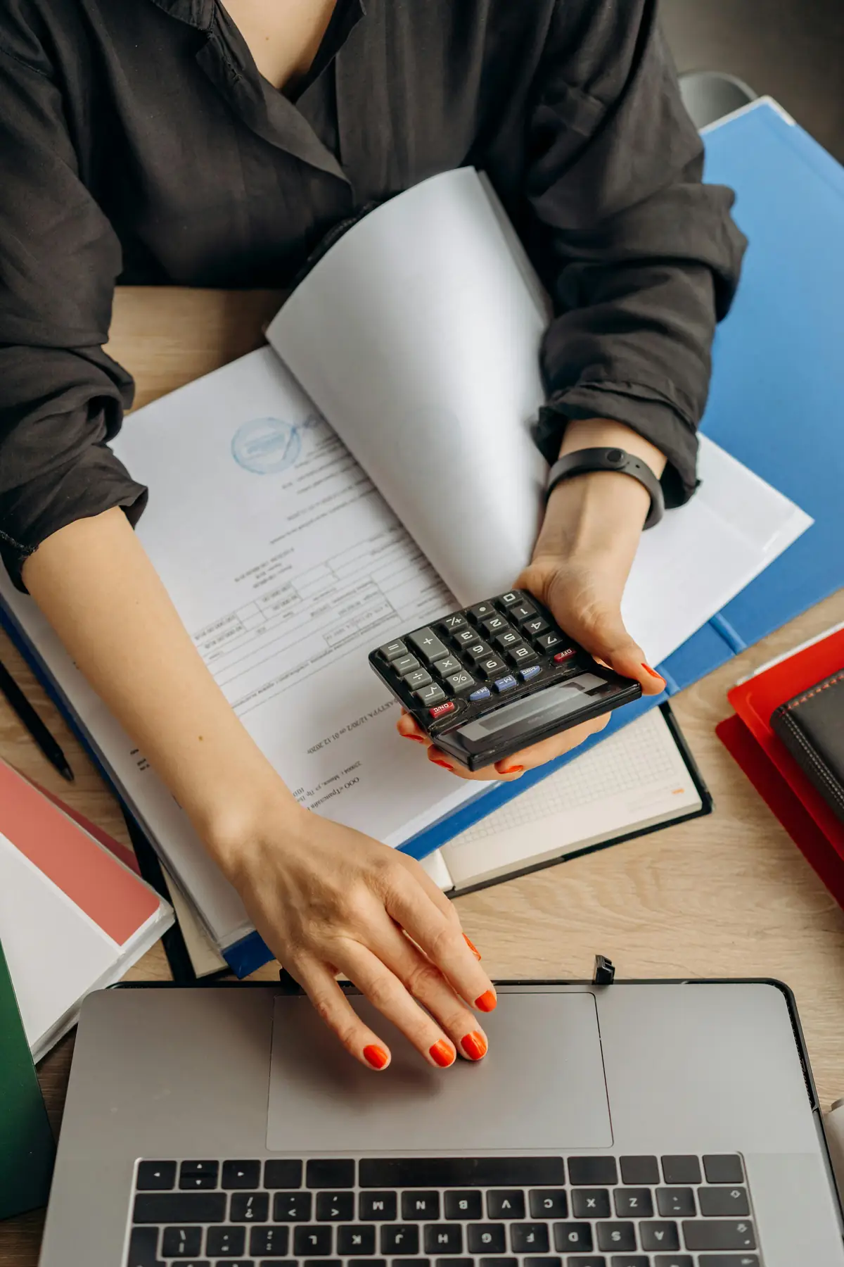 Person using a calculator beside a laptop and files, analysing costs along Porter's value chain