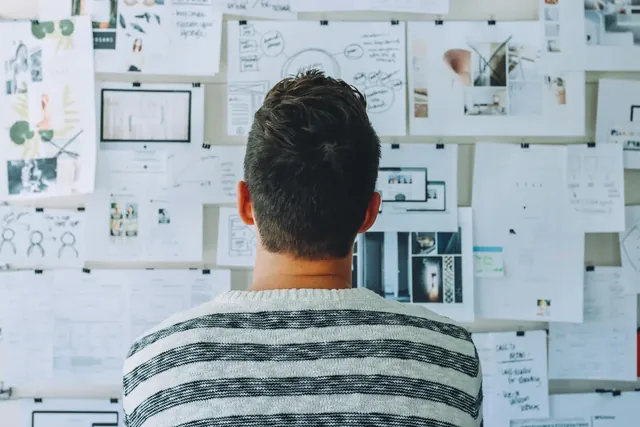 Designer betrachtet von hinten eine Wand voller Skizzen und Notizen während der Ideenfindung im Design Thinking