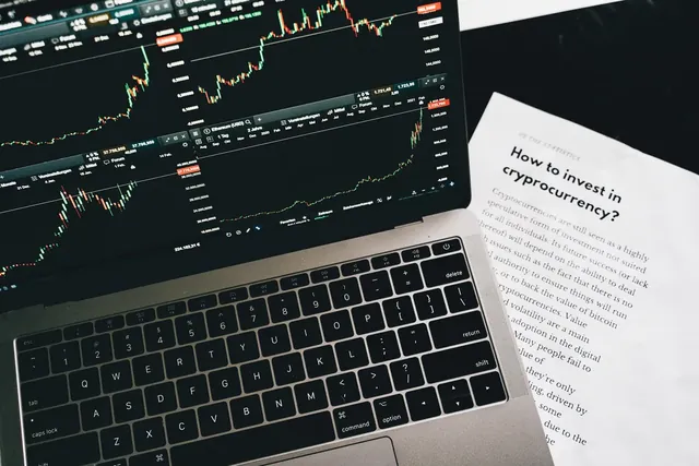 Laptop mit Kursdiagramm neben einem gedruckten Investment-Ratgeber, Sinnbild für die Wahl zwischen Red Ocean und Blue Ocean