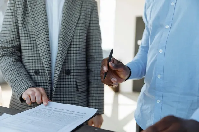 Zwei Kollegen in Businesskleidung gehen gemeinsam ein ausgedrucktes Dokument zur Planung eines Pilotprojekts durch