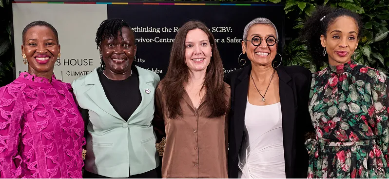 Five diverse women standing side by side smiling in front of a backdrop with text about rethinking SGBV survivor-centres.