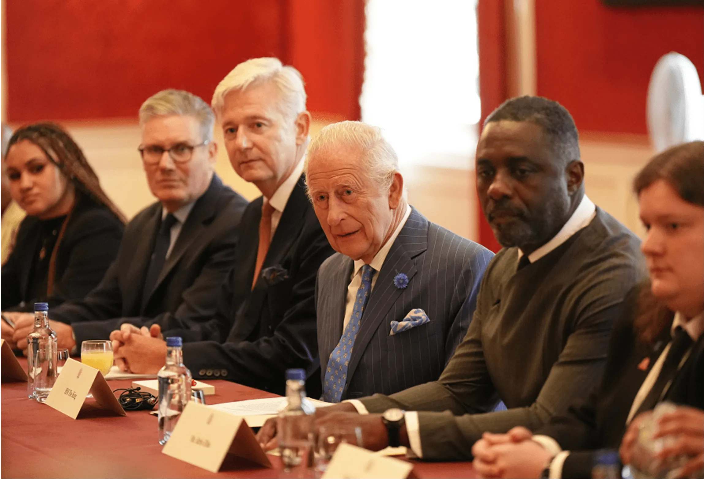 Six people seated at a conference table with papers, water bottles, and nameplates in a formal meeting room.