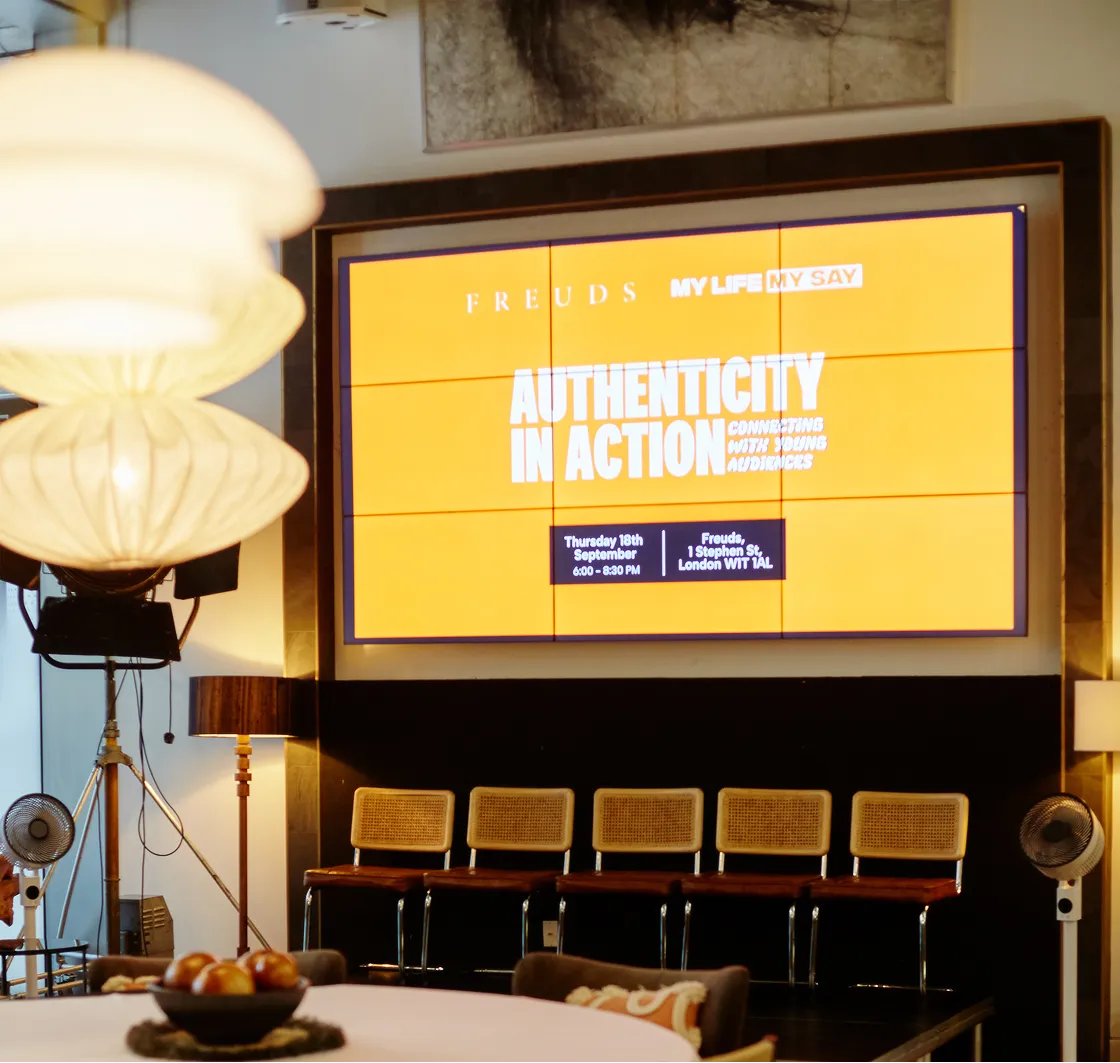 Event space with a large screen displaying 'Authenticity in Action' and event details, with a row of chairs underneath.