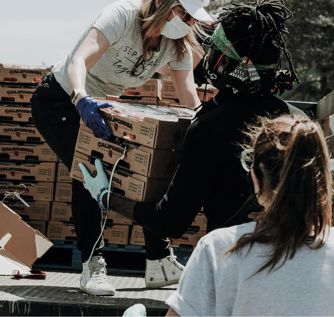 Three people wearing masks and gloves loading boxes of California strawberries into a truck.