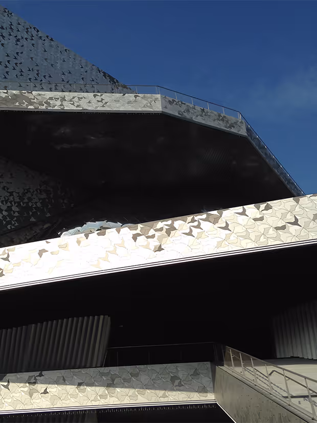 Vue en contre-plongée d'un bâtiment contemporain avec façades en métal géométriques par Aude de Prisme (COO Fractionelle)