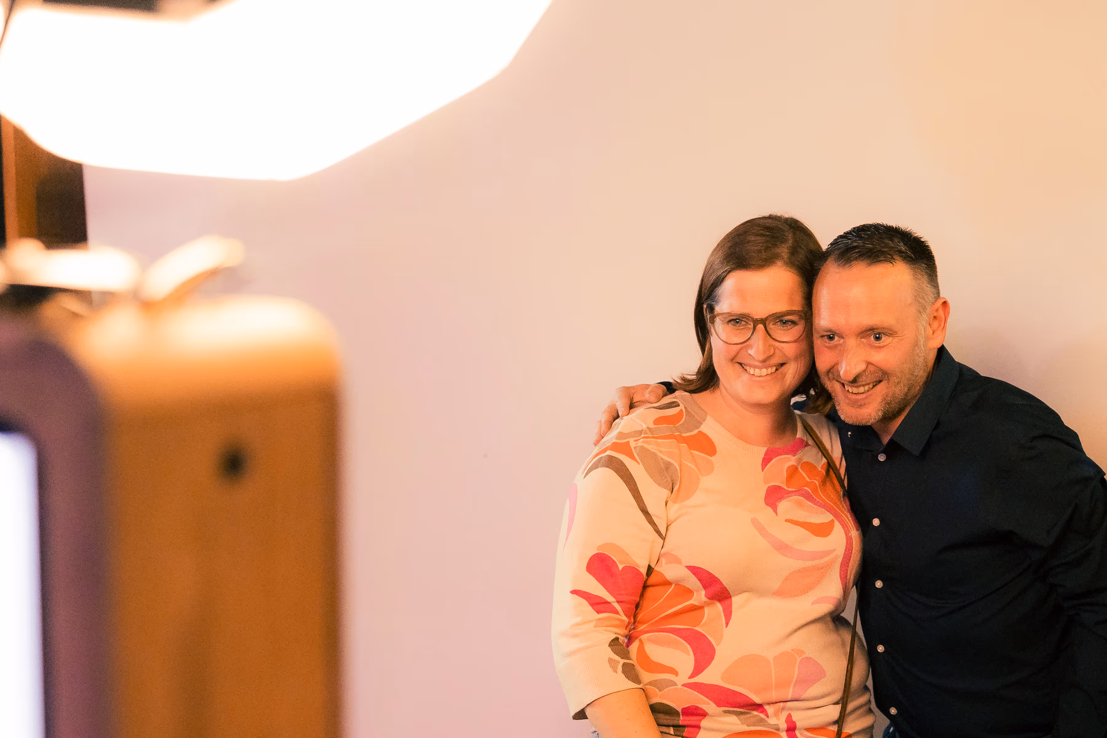 Twee personen glimlachend poseren samen voor een foto met een effen achtergrond.