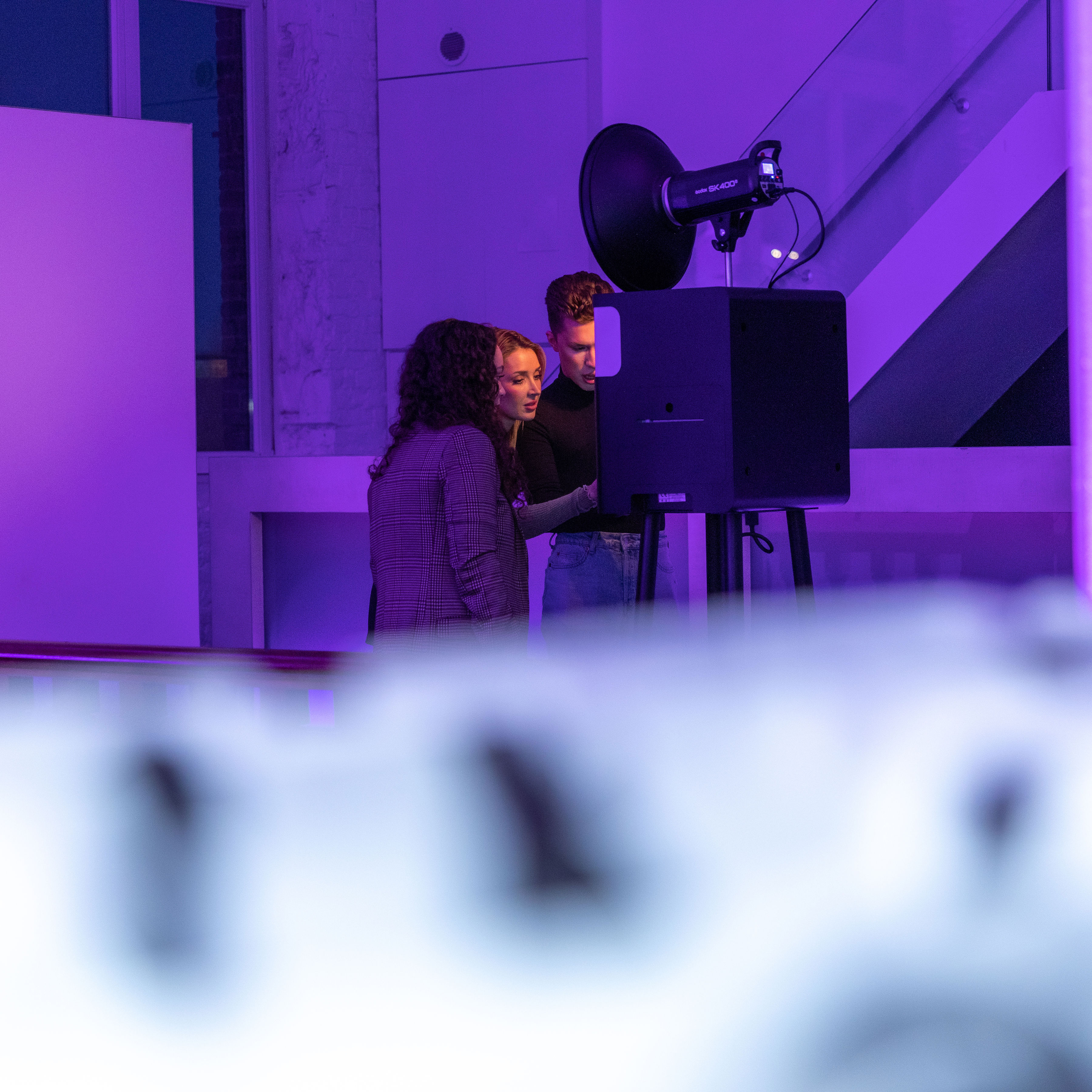 Drie jonge volwassenen bekijken iets samen achter een fotostudioverlichting in een modern interieur met paarse verlichting.