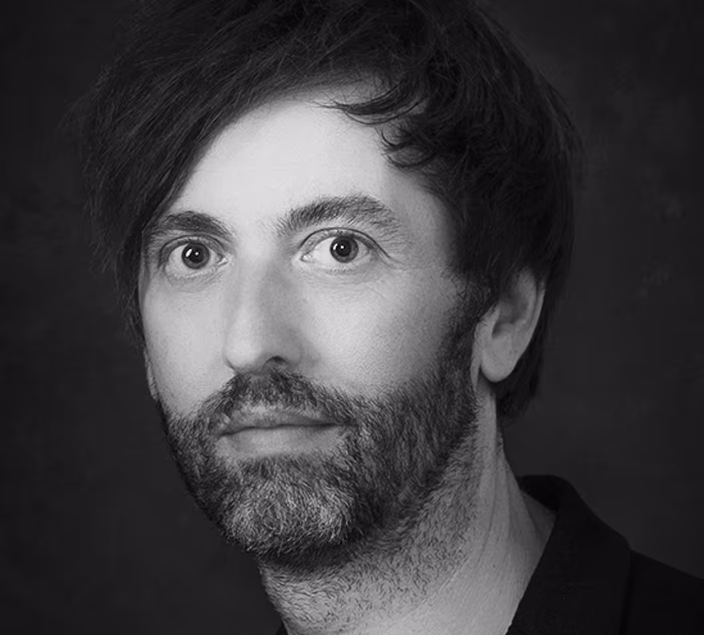 Zwart-wit portret van een man met donkere, lichte baard en kort haar, kijkend naar de camera.